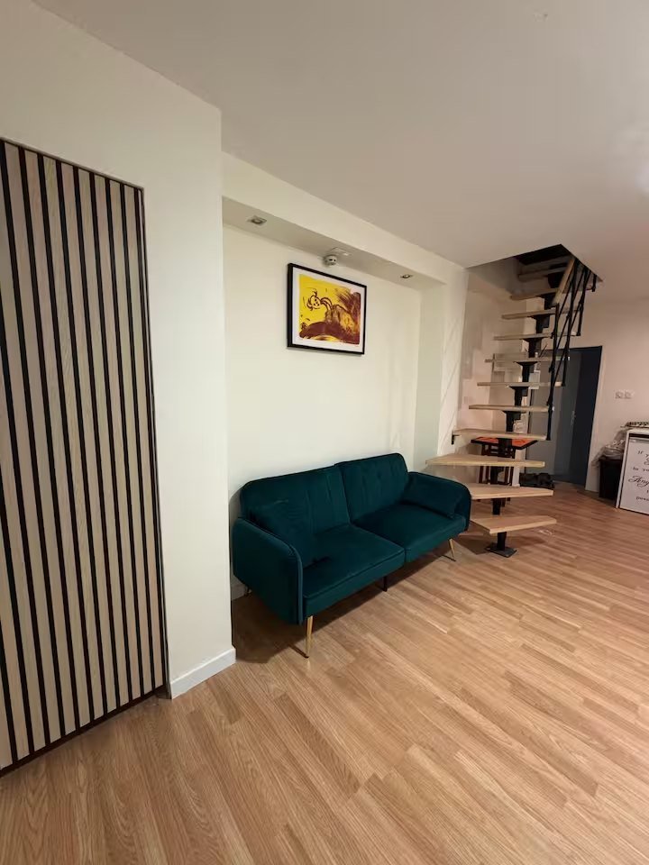 Coin salon avec canapé vert canard, mur à lattes de bois et escalier menant à l'étage